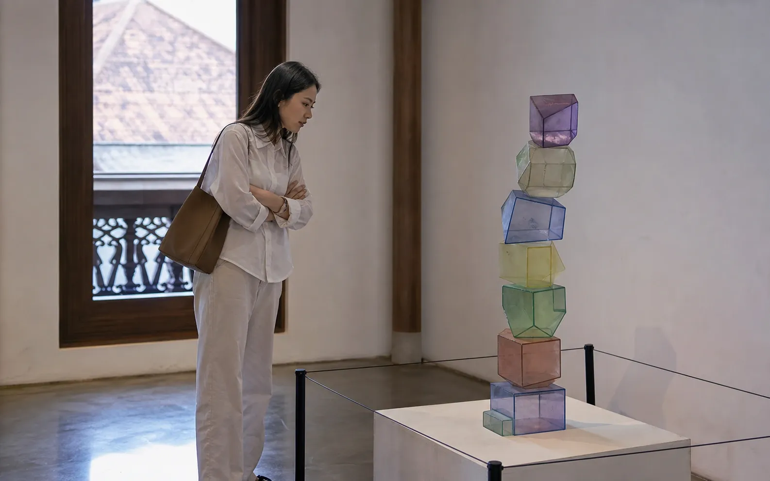 Pengunjung mengamati tumpukan token geometris tidak stabil di balik pembatas museum